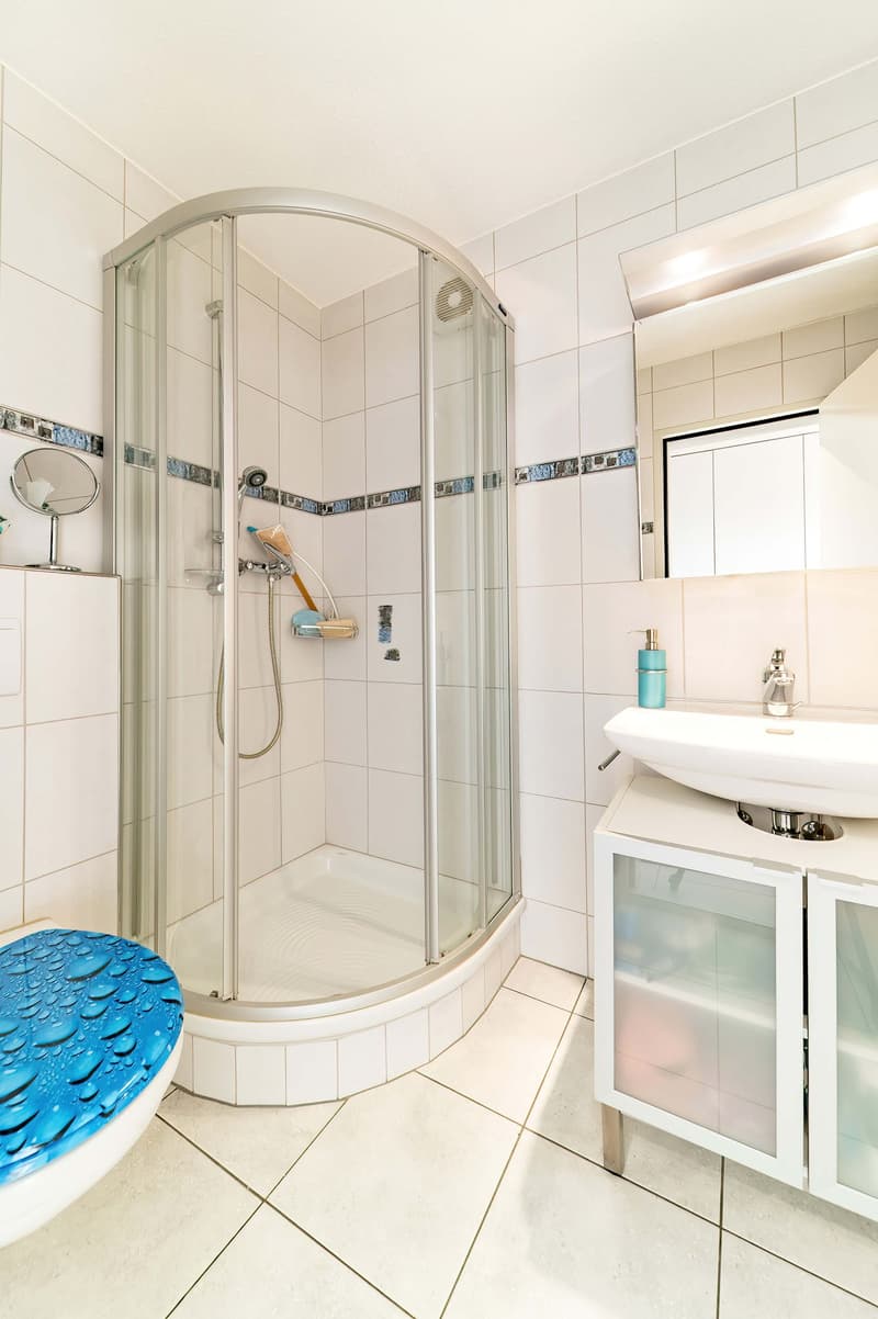 modern bathroom with shower, sink, toilet, mirror, and storage cabinet