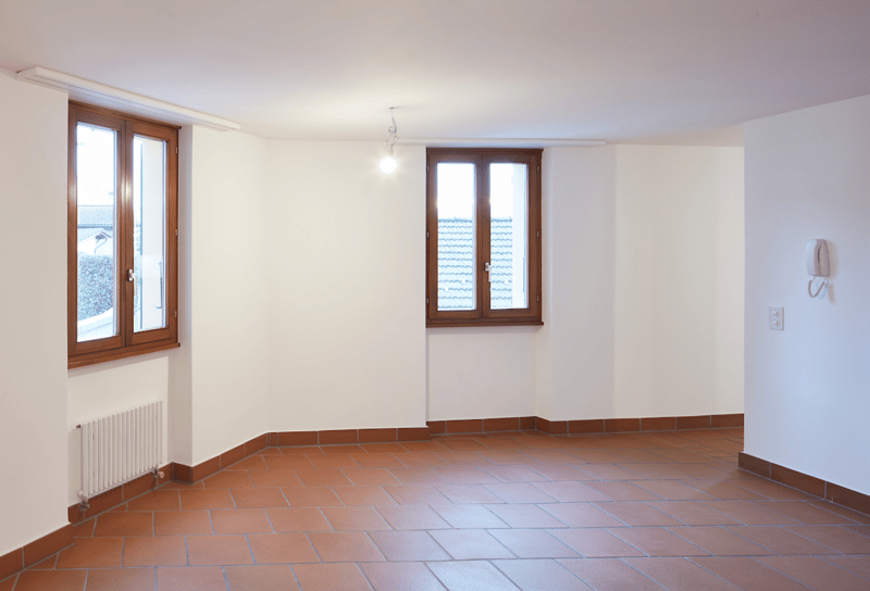 two windows, white walls, red tile flooring, heater mounted on wall, no furniture