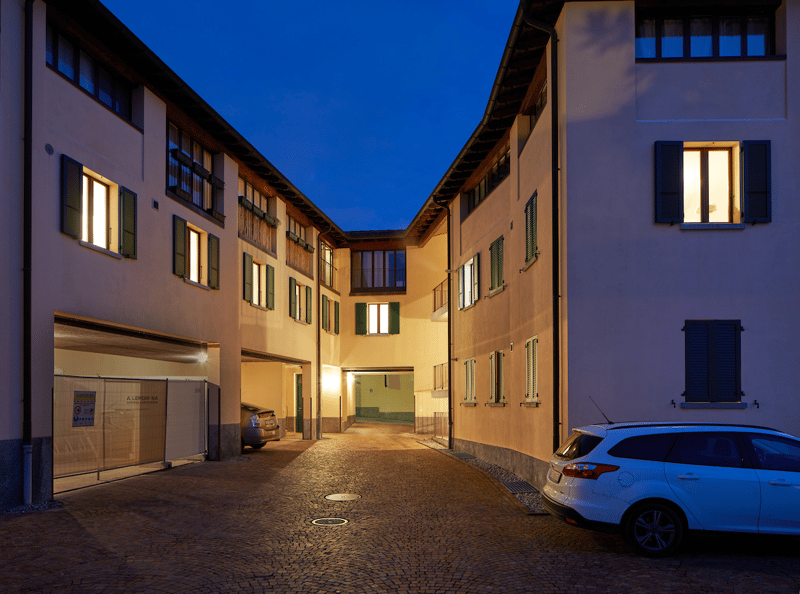 Illuminated building at night, multiple windows and doors, entrance to a garage, a car parked