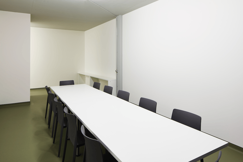empty conference room with a long white table and black chairs, white walls, gray floor