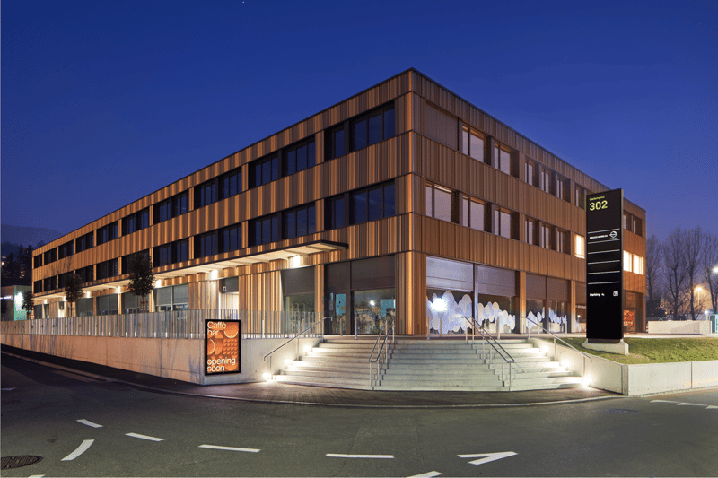 modern multi-story building, brown exterior, glass windows, ground-level storefront, stairs, parking sign