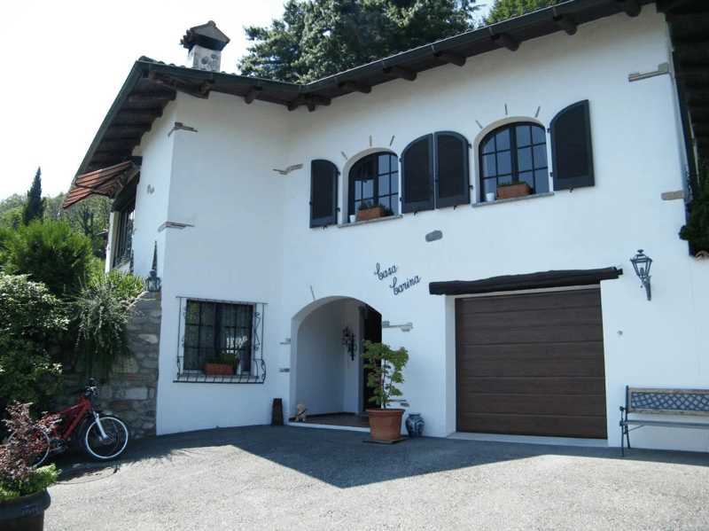A white house with stone wall, white windows, garage, arched entrance, bench, and potted plants.
