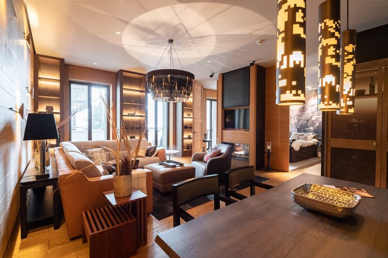 Fireplace, chandelier, couch, armchairs, side table, coffee table, rug, lamps, wooden floor, wood-paneled walls