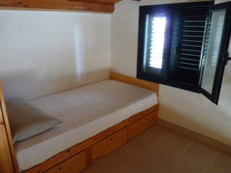 single bed with drawers, wooden bedframe, white sheets, pillow, open window with shutters, white walls, tiled floor
