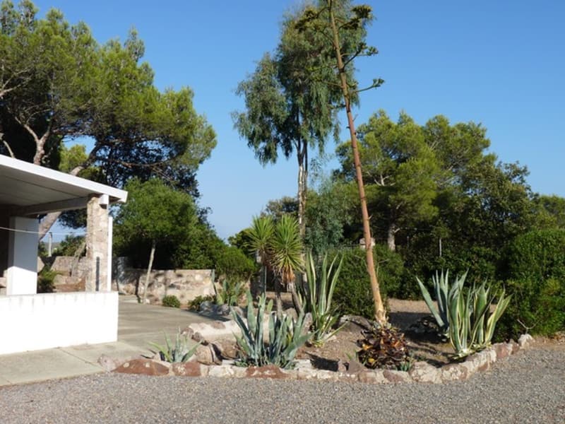 Stone wall, gravel, trees, plants, car parked under covered area, clear sky