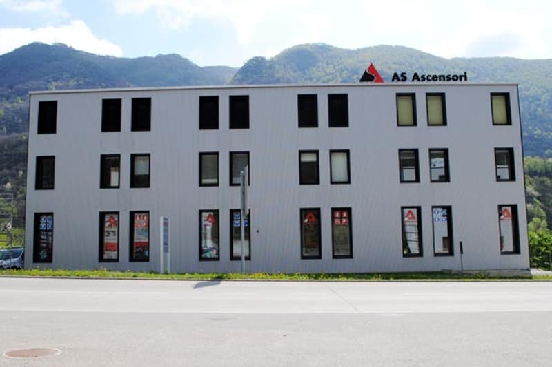 A multi-story commercial building with a gray exterior and large windows. The building has the name 'AS Ascensori' displayed on the facade.