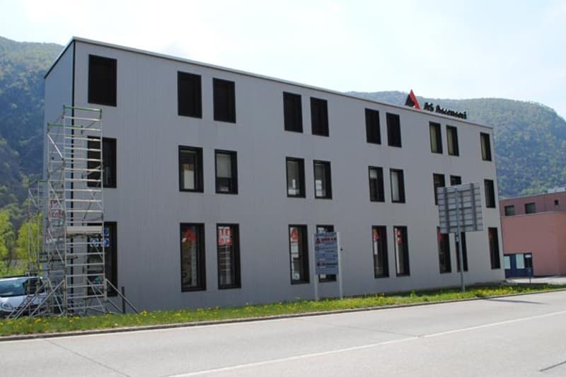A multi-story commercial building with a gray exterior and large windows. The building appears to be a modern office or retail space located in a mountainous area.