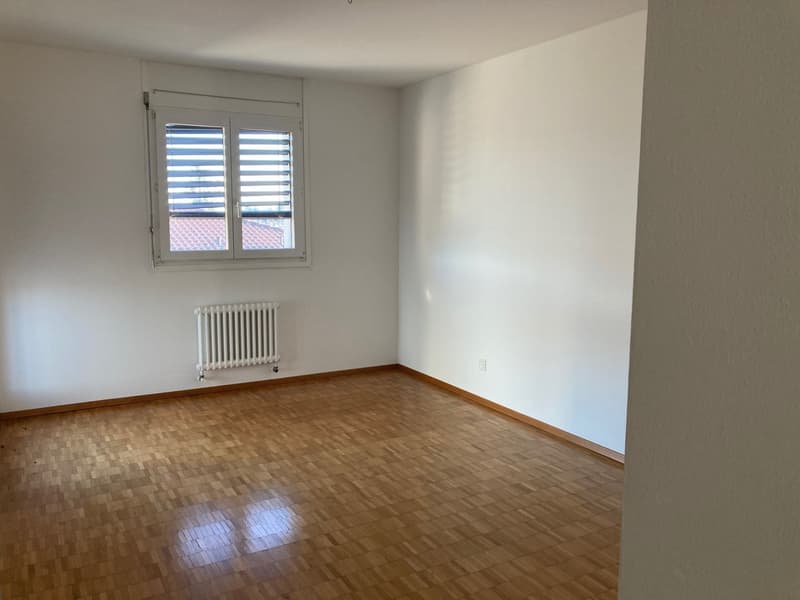 Empty room with wooden floor, white walls, a window with blinds, and a white radiator