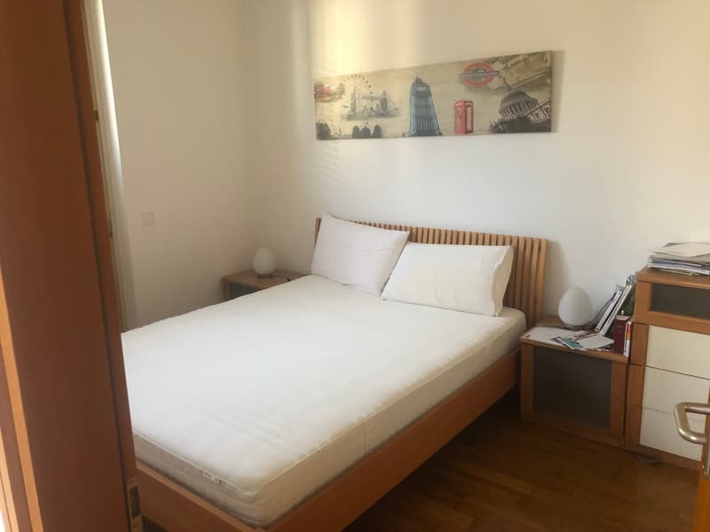 A simple bedroom with wooden bed, nightstands, and painting on the wall. There are two nightstands with lamps on each side of the bed.
