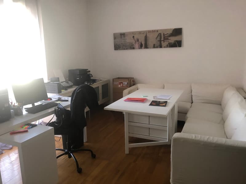 white walls, white desks, black office chair, L-shaped white couch, wooden floor, wall art