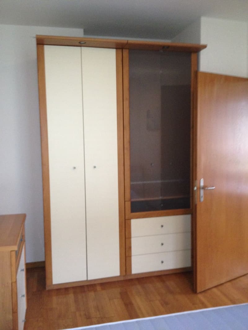 Large wooden wardrobe with glass doors, two smaller wooden drawers in the bottom section, wooden floor, wooden nightstand with drawers