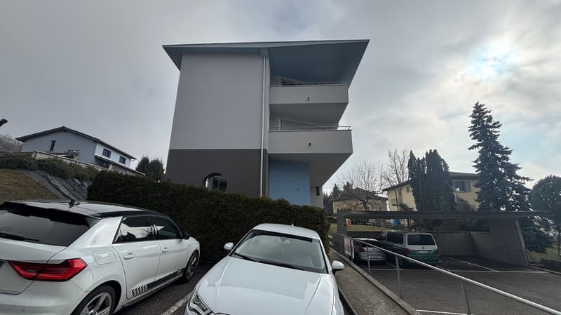 A modern, raised ground floor building with balconies, a parking garage, and several cars parked