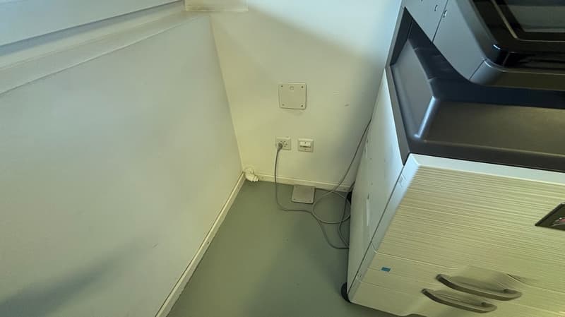 Corner of room, white walls, gray floor, power outlets, office equipment