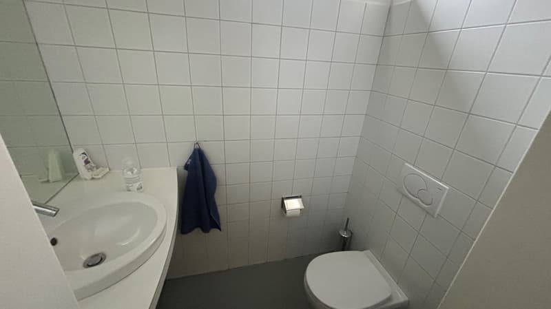 a white bathroom with a sink, toilet, mirror, towel, and tiled walls