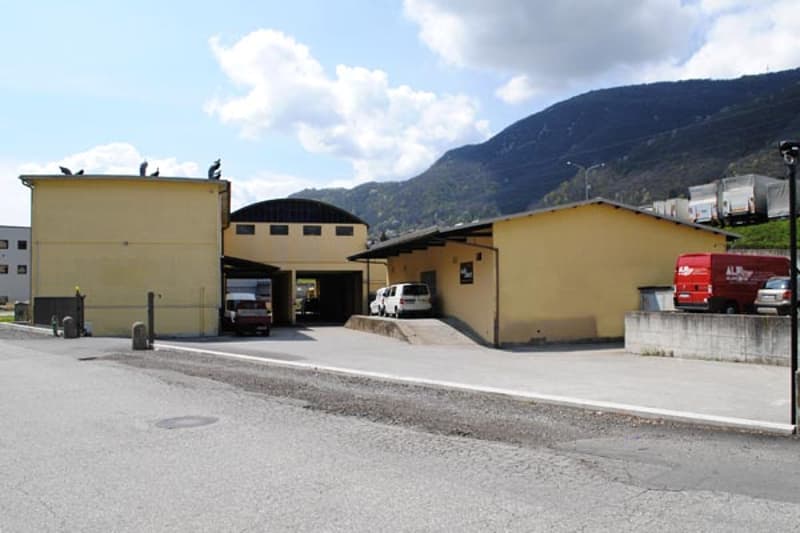 Large yellow building with multiple garages, vehicles parked in front, mountains in the background