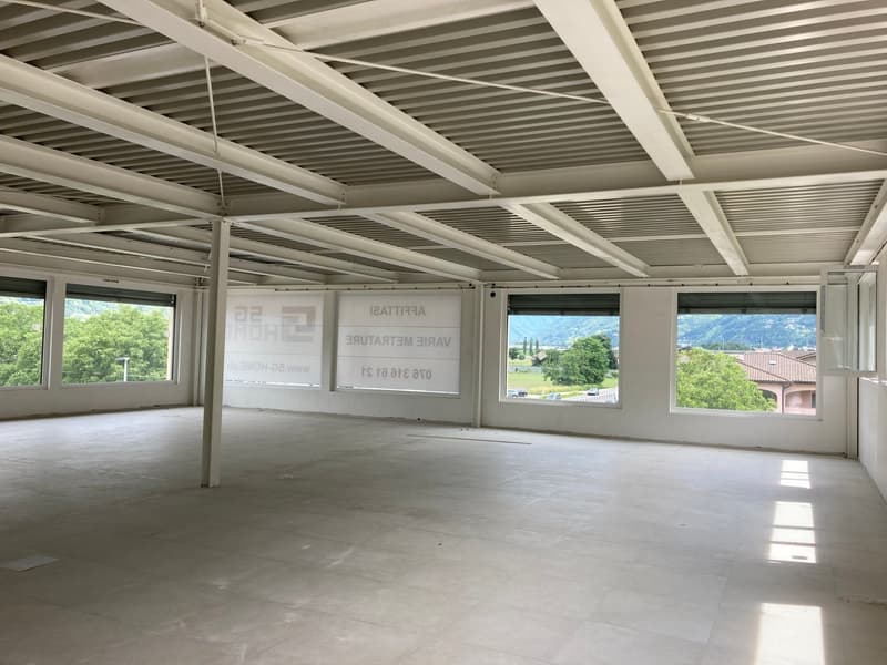 Empty room with white walls, white ceiling, large windows, tiled floor, and a view of the outside