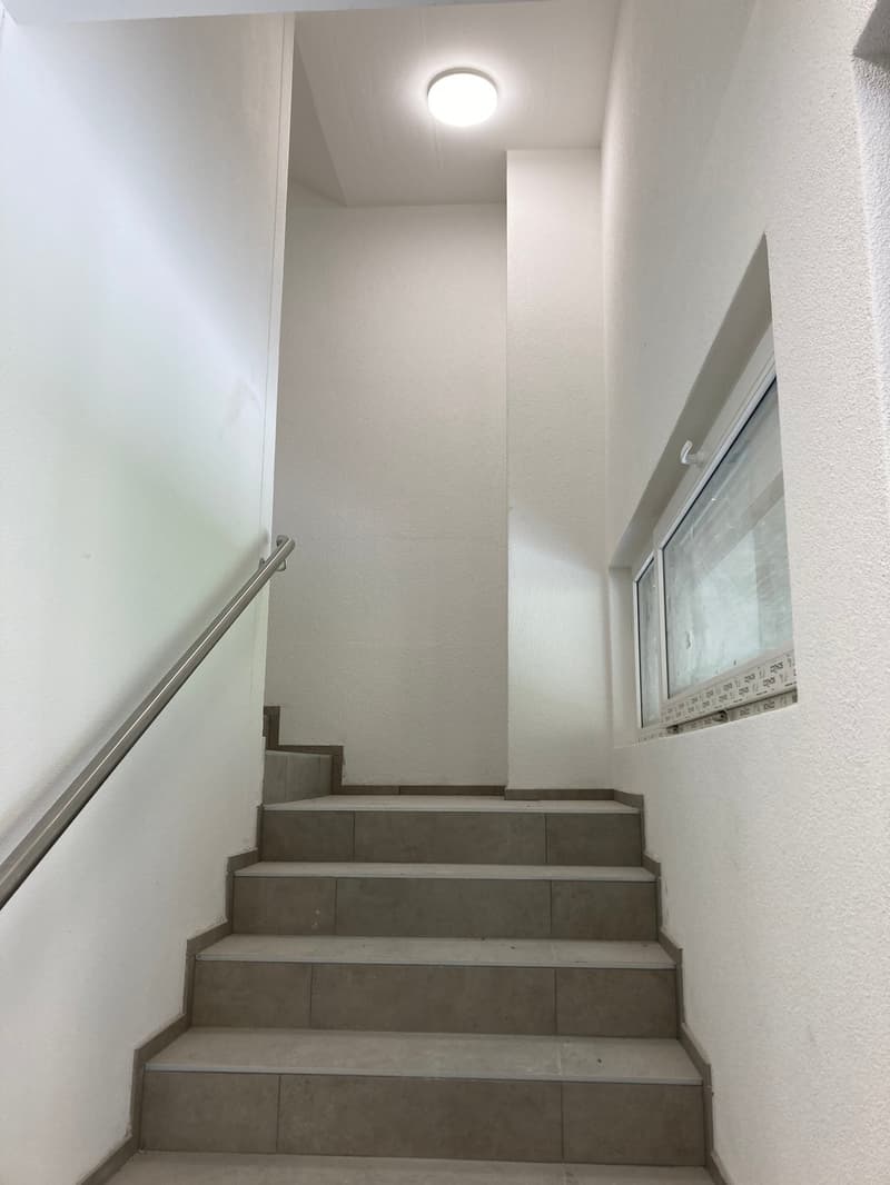 white walls, gray tiled steps, metal handrail, circular ceiling light