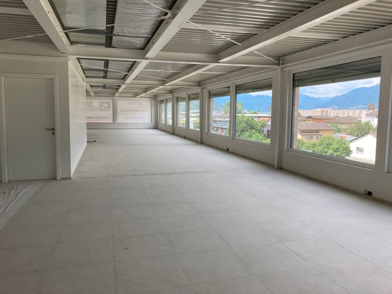 Empty room with white tiles, large windows, metal ceiling, and a door.