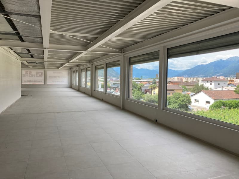 Empty room with large windows, tiled floor, metal ceiling, view of mountains and buildings