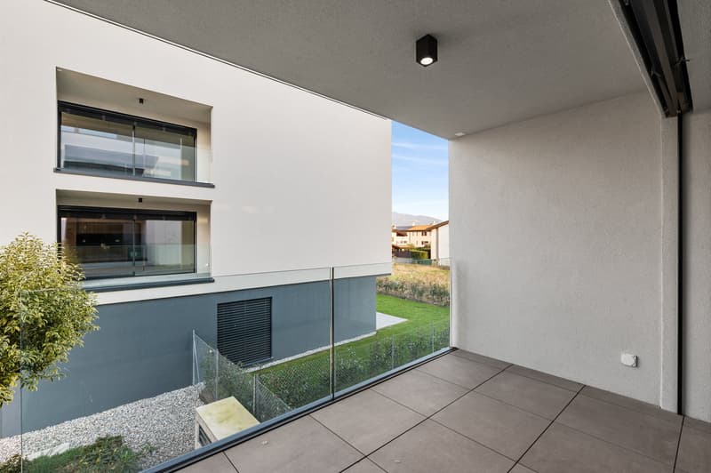 Two-story apartment with large windows, glass balcony railing, and a view of the surrounding landscape and buildings.