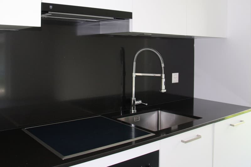 modern kitchen with induction hob, stainless steel sink, faucet, black granite countertops, white cabinets, power outlet