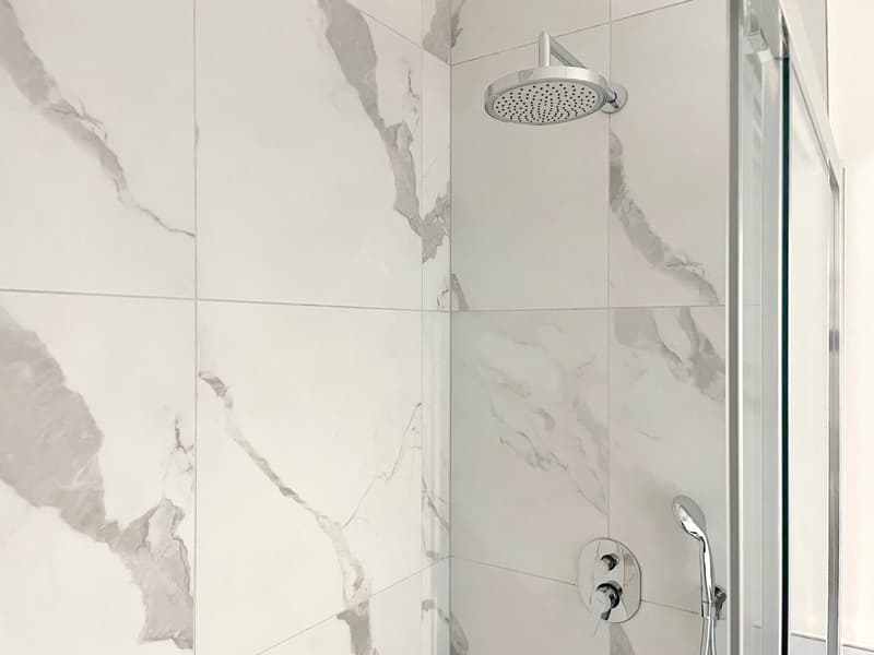 white tiled walls, silver shower head, clear glass enclosure, handheld shower head, chrome fixtures
