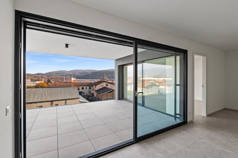 Sliding glass door leading to a balcony, tiled floor, panoramic windows, distant buildings and mountains