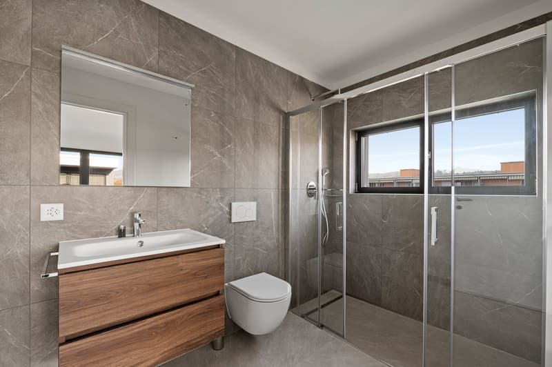 White toilet, modern sink, wooden vanity, marble tiled walls, modern shower enclosure, white and grey tiles