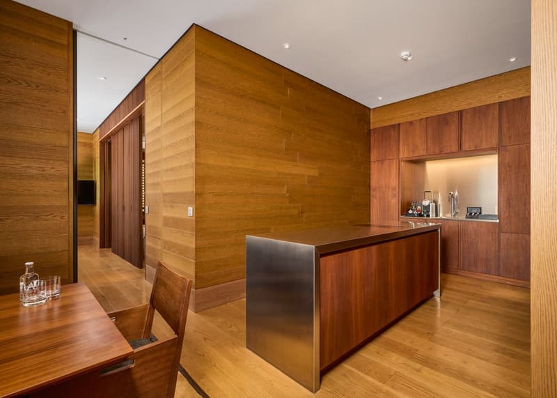 modern kitchen with wooden walls, stainless steel countertop, wooden cabinets, wooden table, chair, and a bottle on the table