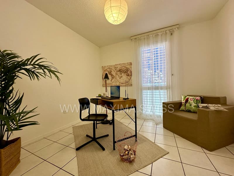 minimalist room with desk and chair, brown sofa with pillow, white tile flooring, and plant in a basket