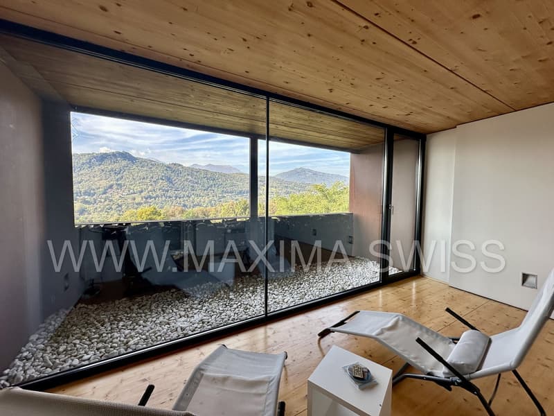 Large glass walls, wooden floor, balcony with pebble pathway, white walls, large windows, white lounge chairs