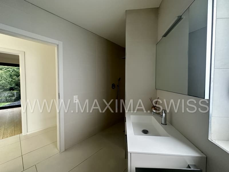 Bathroom: tiled floor, large mirror, white cabinet with sink and faucet, shower area, open door leading to another room