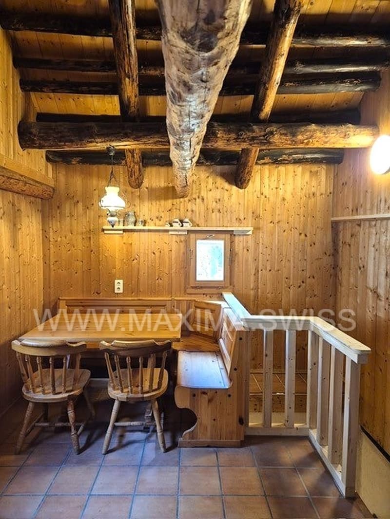 small dining area with wooden dining table, 4 chairs, wooden bench, wooden ceiling beams, tiled floor, hanging light