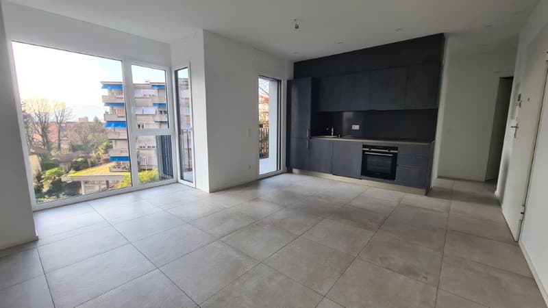 Open-concept living room and kitchen with large windows, modern black kitchen cabinets and appliances, and access to a balcony or terrace.