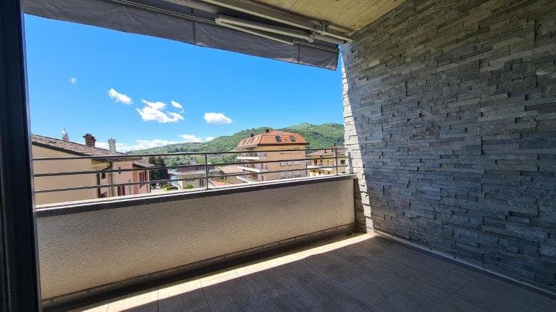 An empty balcony with a view of the city and mountains, featuring a brick wall and wooden floor.