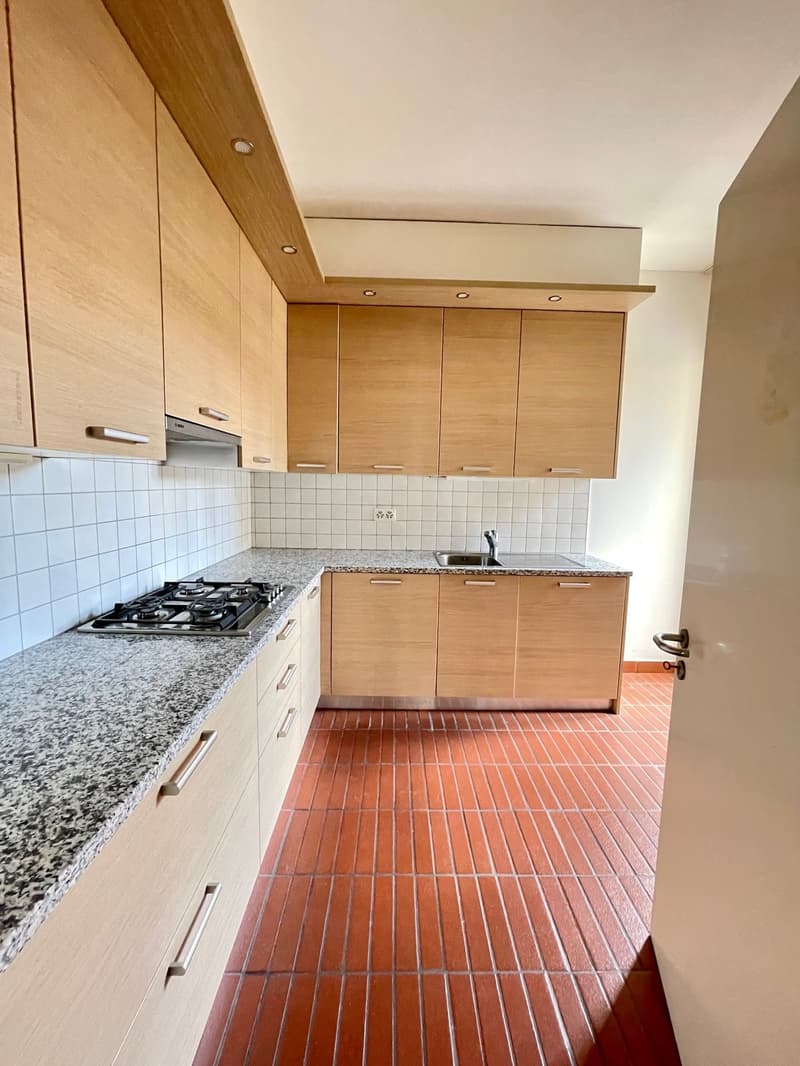 modern kitchen with wooden cabinets, granite countertops, stainless steel appliances, gas stove, and red tiled floor