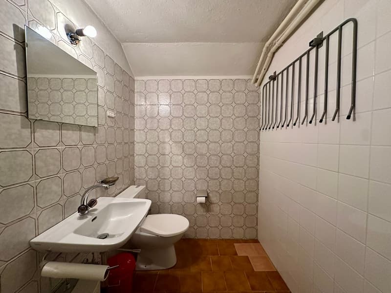 small bathroom with white tiles, white sink, white toilet, mirror, and towel rack