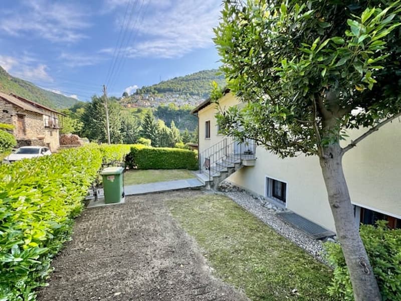 A single story house with a driveway, green trash bin, and stairs in front. Mountain backdrop.