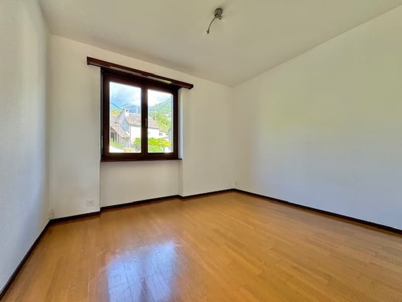 Empty room with wooden floor, large window, white walls