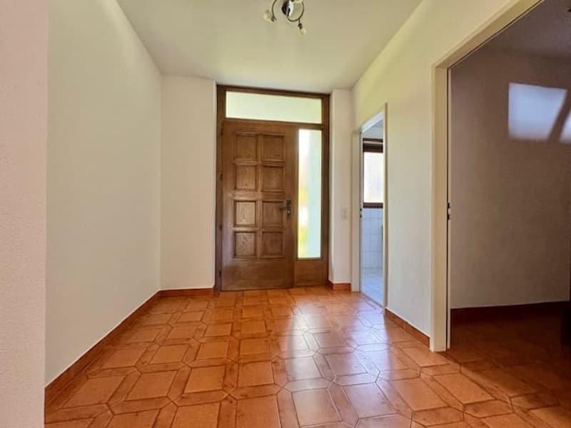 Entrance hall with wooden flooring, a brown wooden door, white walls, and a glass window to the left of the door. The room is currently empty.