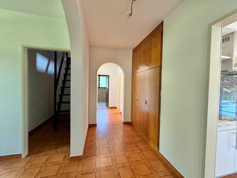 long hallway, wooden flooring, white walls, stairs leading up to upper floor, arch passageway