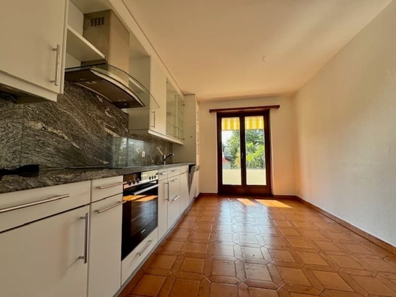 Modern kitchen with tiled floor, white cabinets, marble countertop, oven, and a balcony