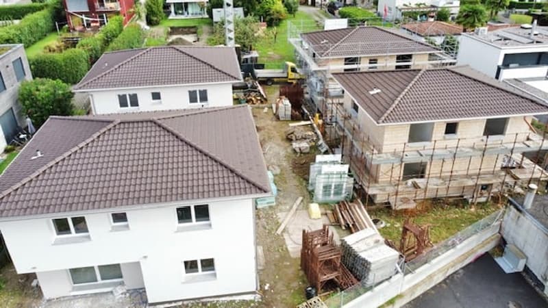 4 houses in different stages of construction, brown roof tiles, brown and white walls, many windows, surrounding greenery