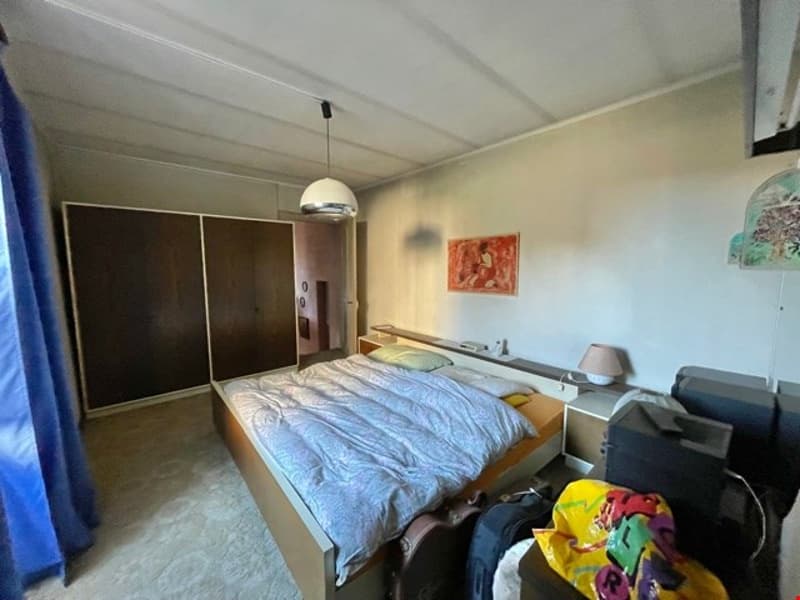 Bedroom with a bed, bedside tables, wardrobe, carpet, lamps, picture frame, blue curtain, suitcases