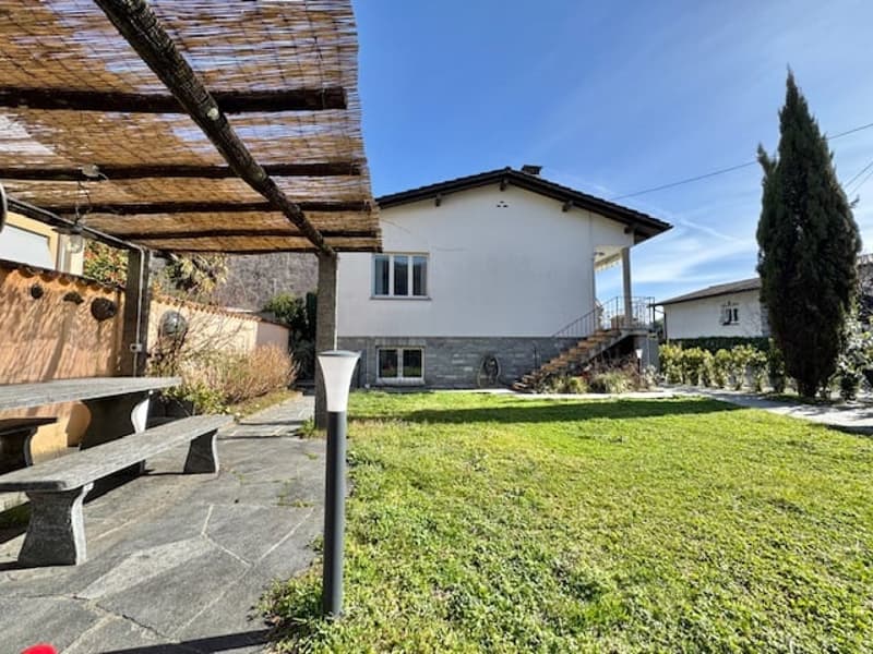 2-story white house with stone exterior, covered patio area, grassy yard, and parking space