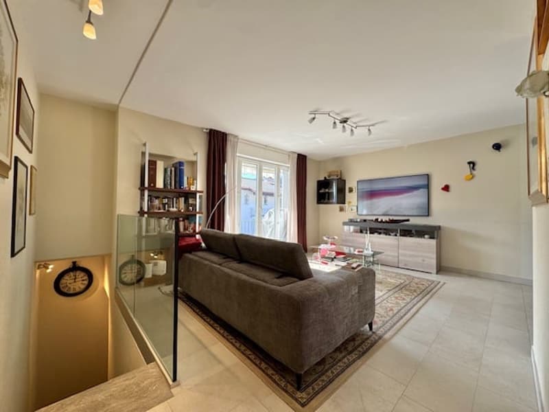 Spacious living room with large windows, hardwood floors, brown sofa, TV stand, and shelving unit