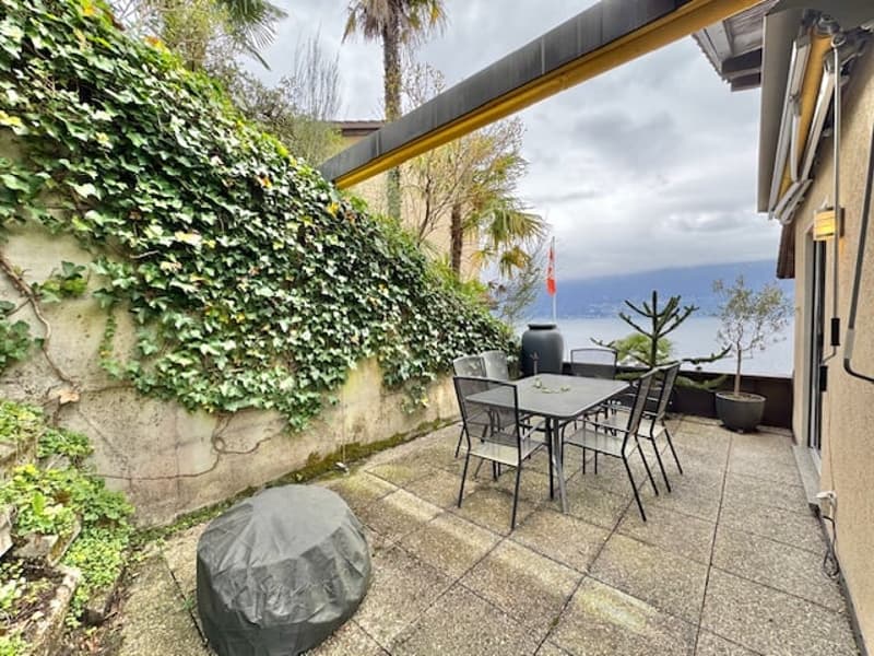 Outdoor patio with a dining table and chairs, covered by a roof, covered with plants, table cover, with a lake view.
