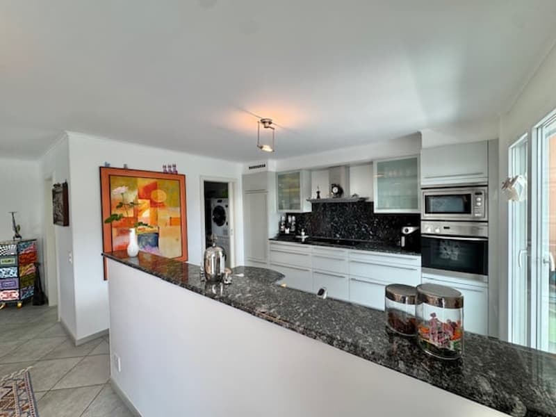 Spacious kitchen with white cabinets, granite countertops, built-in appliances including a dishwasher, and a colorful abstract artwork on the wall.