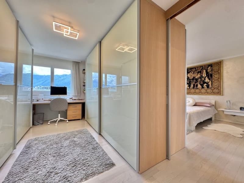 Spacious bedroom with large windows, wooden furniture, desk, and a separate seating area
