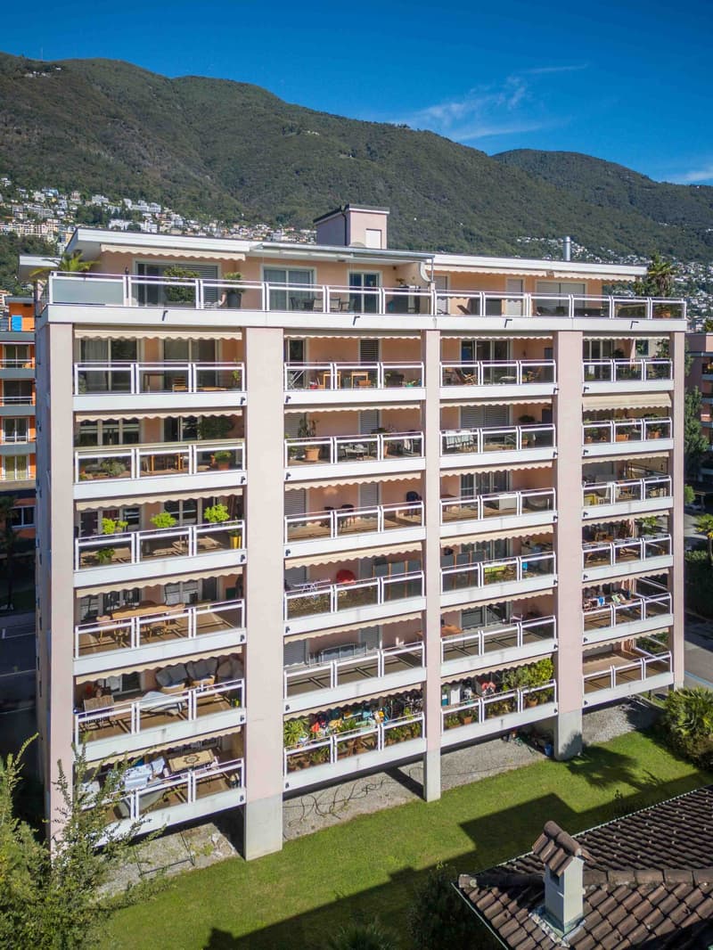 High-rise apartment building, multiple balconies on each floor, surrounded by greenery, scenic mountain view